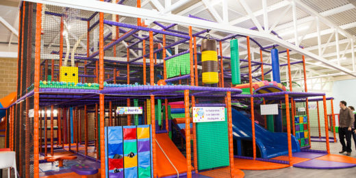 A colorful indoor play structure featuring multiple slides, climbing areas, and soft play elements. The design includes vibrant purple, orange, and green components, and is suitable for children to explore and play safely.