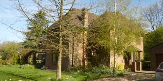 A spacious brick house surrounded by greenery, with a gravel driveway