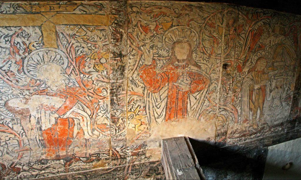 Ancient fresco depicting religious scenes, featuring a central figure of Christ in red robes surrounded by symbolic imagery and figures. The artwork showcases intricate details and vibrant colors, reflecting the historical and cultural significance of the site.