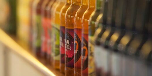 A row of colorful glass bottles containing various beverages, including soft drinks and juices, is displayed on a shelf. The labels feature different designs and colors, showcasing a variety of flavors.