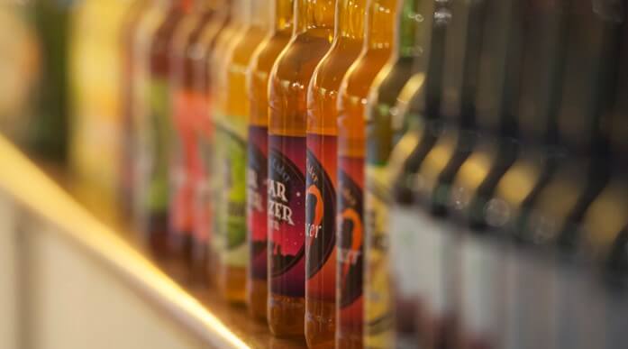 A close-up view of various beverage bottles arranged on a shelf. The bottles display colorful labels, showcasing different flavors and designs, with some in focus and others blurred in the background.