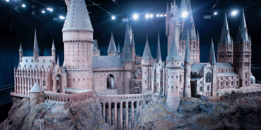 A detailed model of a castle, featuring towering spires and intricate architectural elements, resembles a magical setting. The castle is depicted on a rocky terrain, illuminated by soft lights, creating an enchanting atmosphere.