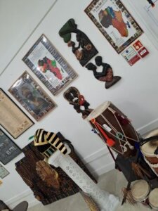 A collection of African-inspired art and musical instruments, including a drum and wooden wall carvings, displayed in a room with framed artworks.