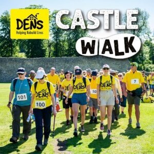 Participants wearing yellow "DENS" shirts walking in a grassy area for the Castle Walk event, organized by a charity focused on rebuilding lives.